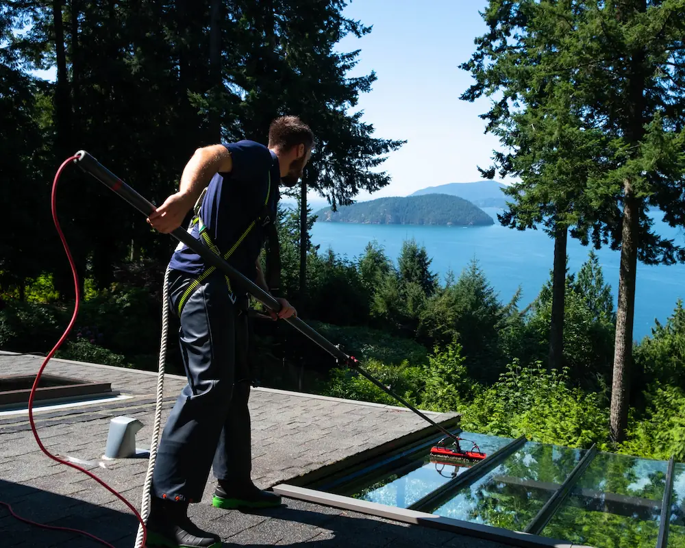 A WashTech technician in a safety harness cleaning glass from a roof