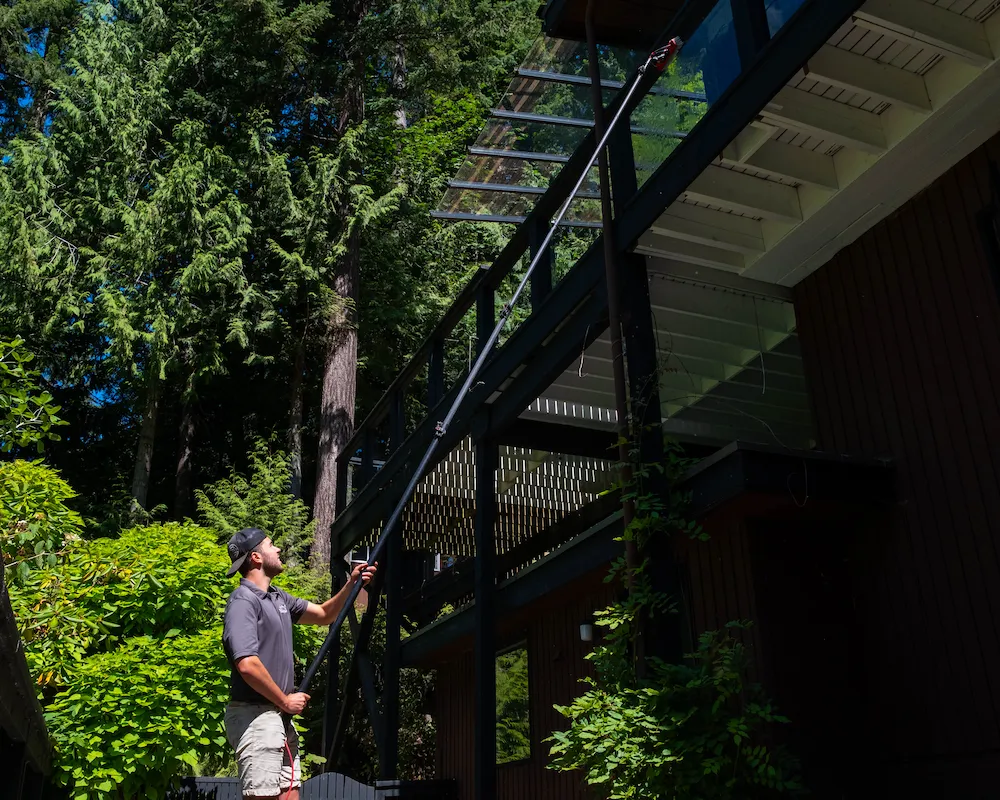 Water-fed pole window cleaning from the ground: a WashTech technician reaches overhead glass on a home